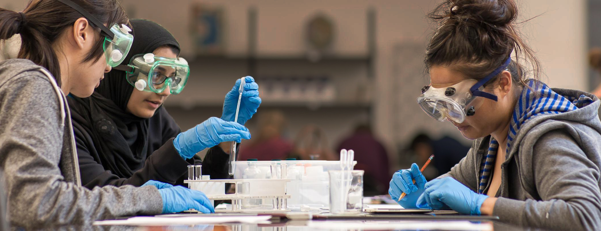  Students wearing safety goggles and gloves in a lab. 