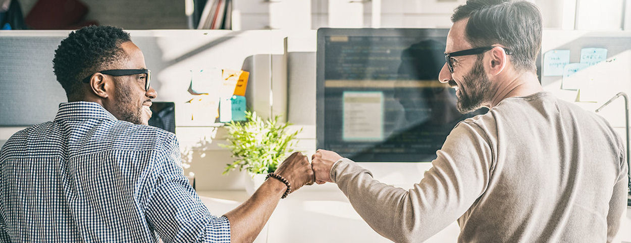 two people at computers giving a fist-bump and smiling