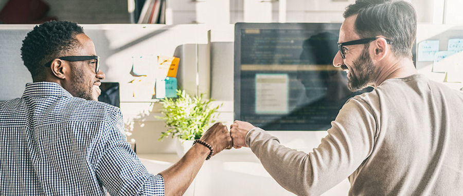  two people at computers giving a fist-bump and smiling 