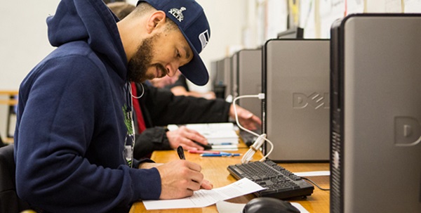  student writing in a notebook near a computer 