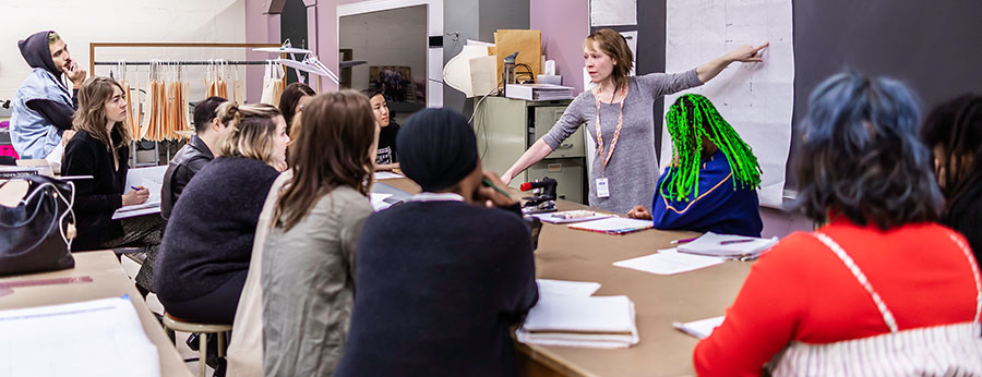  faculty member pointing to a blackboard in a class with students 