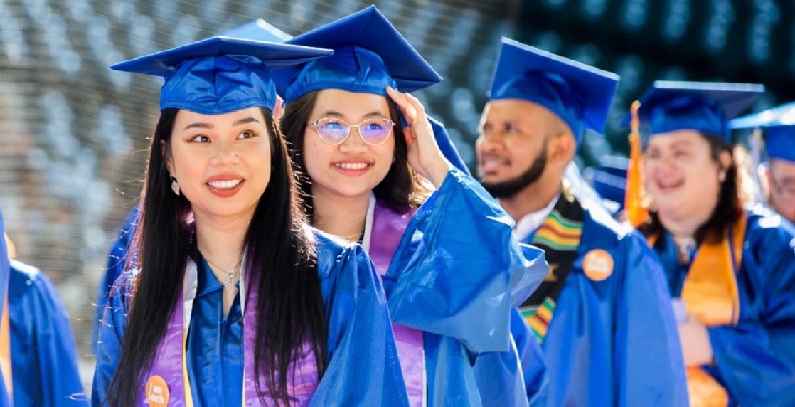  students in line wearing caps and gowns preparing to cross the stage 