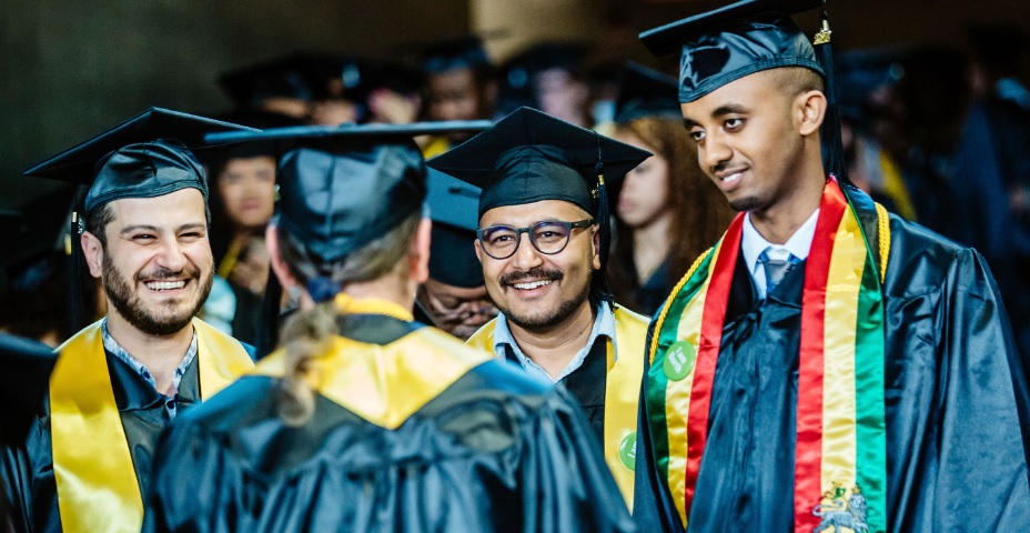  students in caps and gowns smiling and talking with each other 