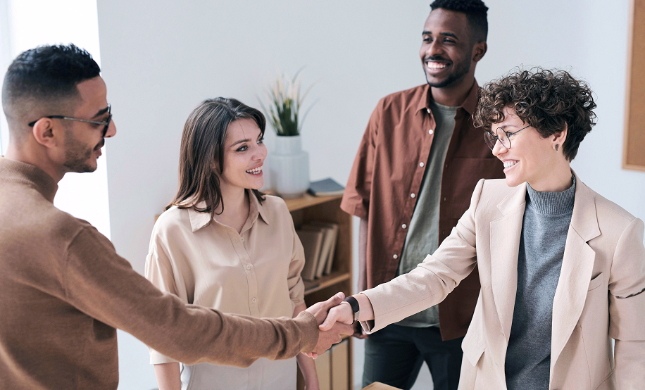 A diverse group of four people smiling and interacting with each other, two of whom are shaking hands