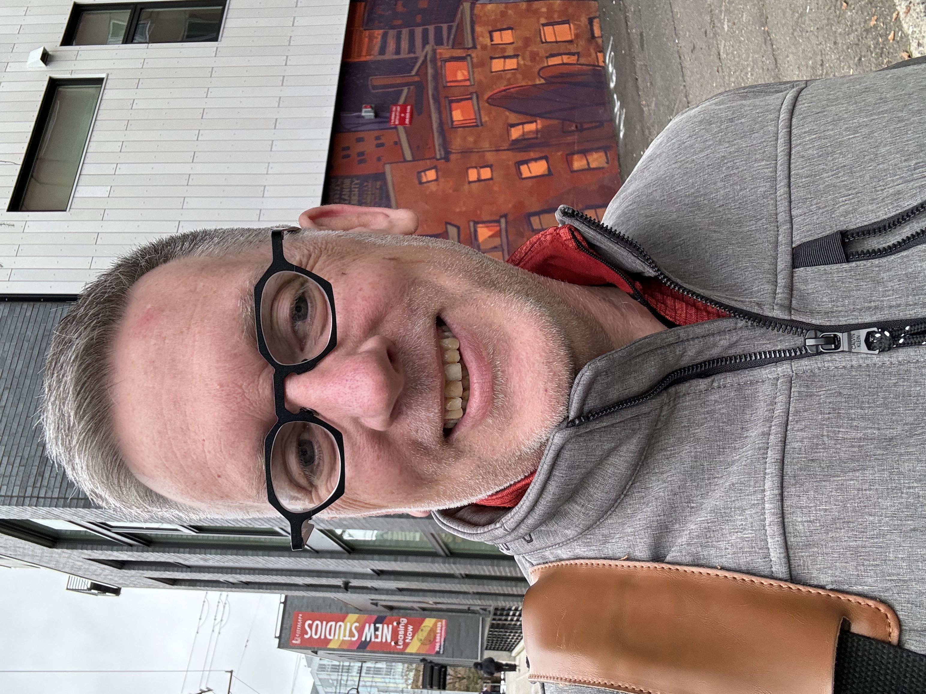 Kevin standing outside with building with painted mural on the wall behind him.
