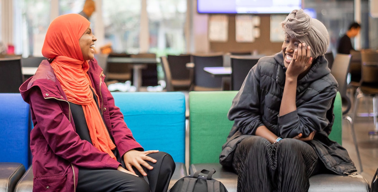 two smiling students in conversation in a campus lounge area