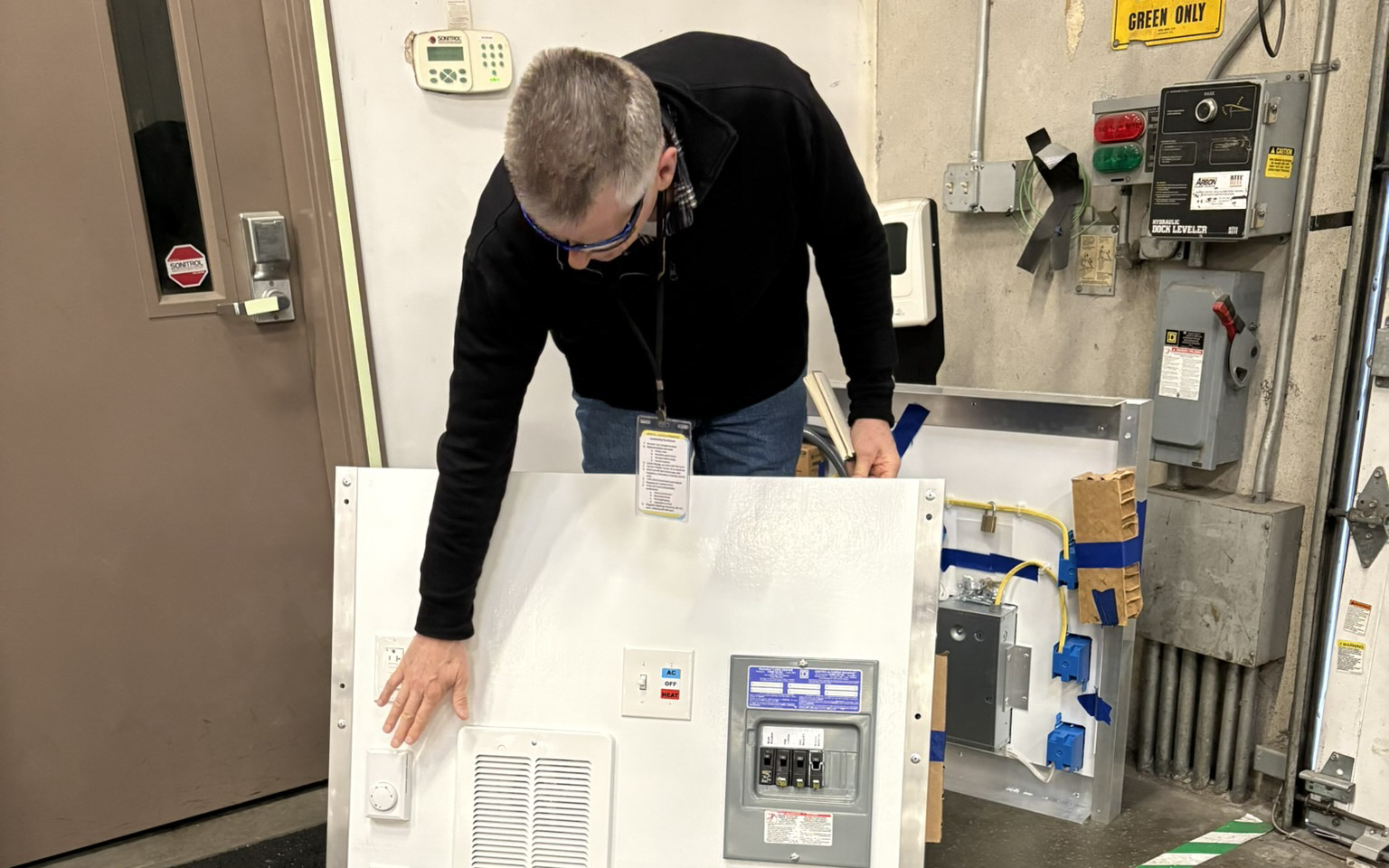 Pallet Shelter representative showcasing the inner workings of a shelter. In the photo, the representative shows an electrical panel, which includes a heating unit.