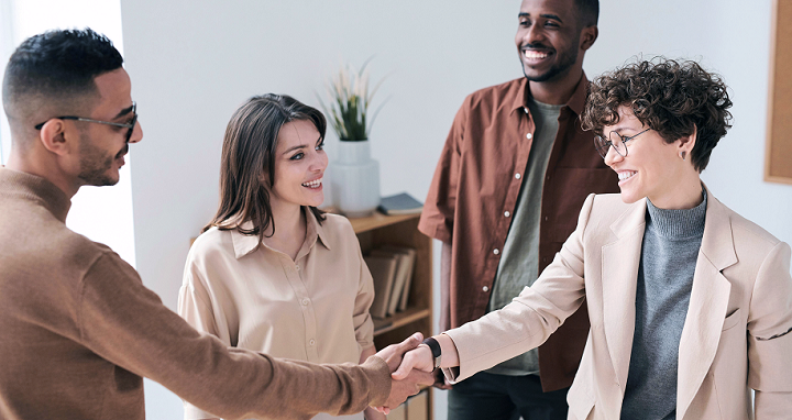 A diverse group of four people smiling and interacting with each other, two of whom are shaking hands