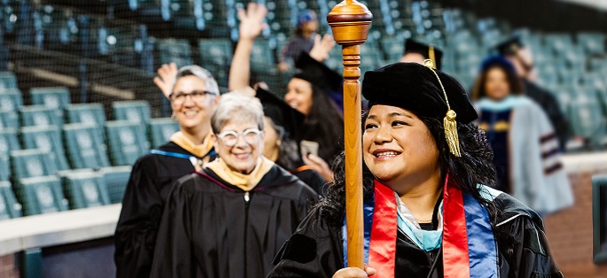 Chancellor Rosie Rimando-Chareunsap holding the academic mace with other college officials at commencement