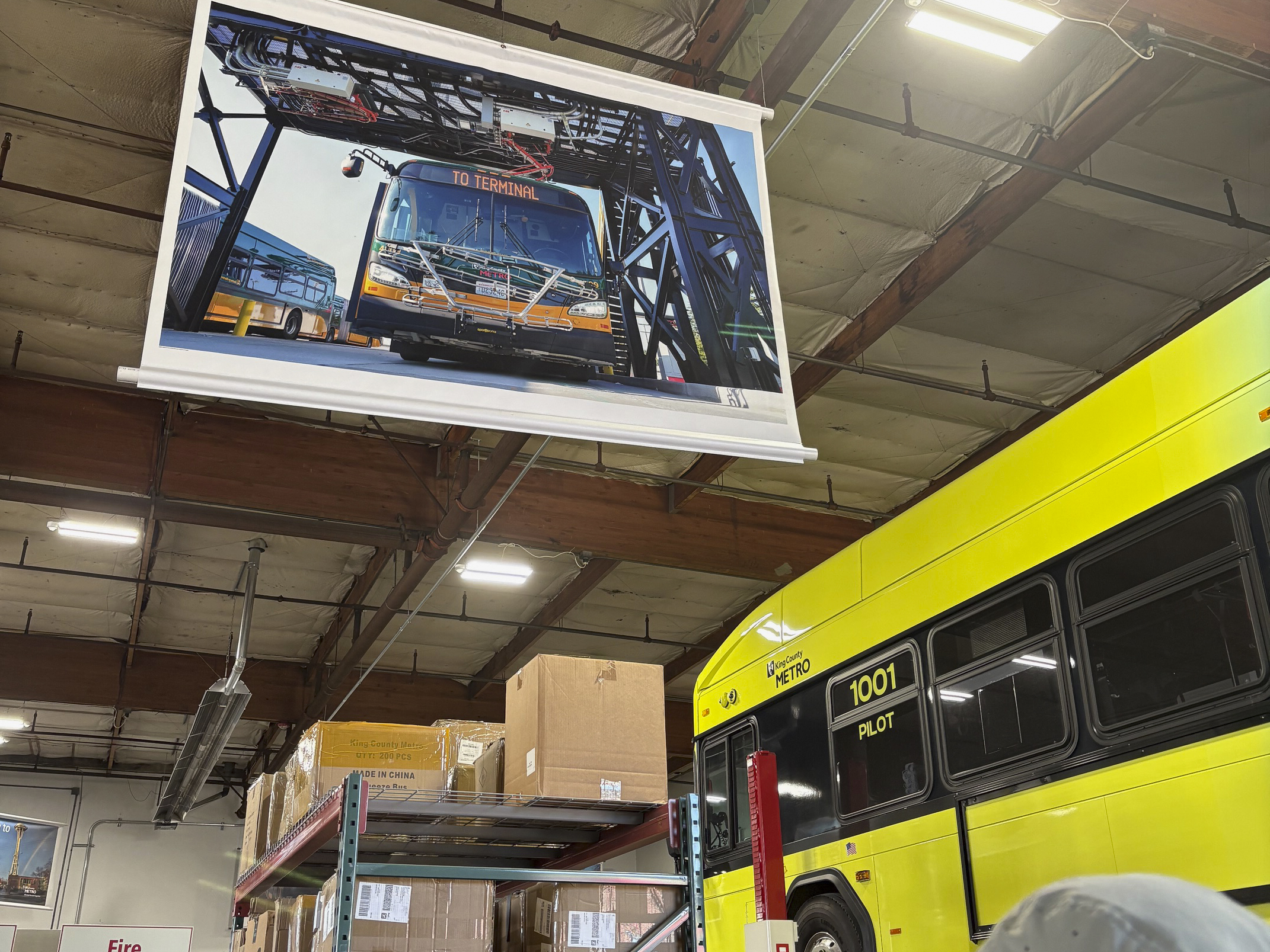 A poster depicting a bus from King County Metro, next to one of the entity's new zero-emissions fleet buses.