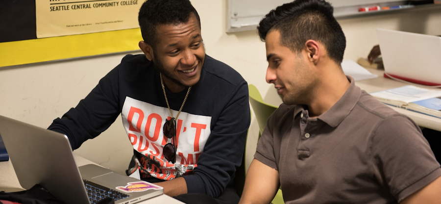 A mentor and mentee smiling and working at a computer