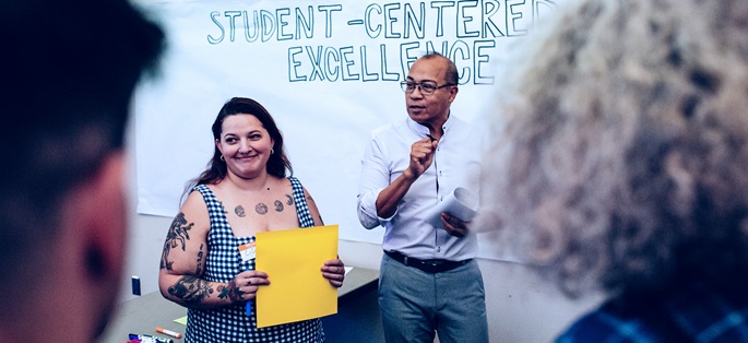 Faculty and staff in a group discussing student-centered excellent, which is on the whiteboard in the background