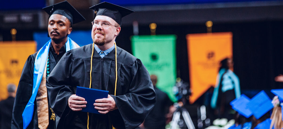 two students wearing caps and gowns after crossing the commencement stage