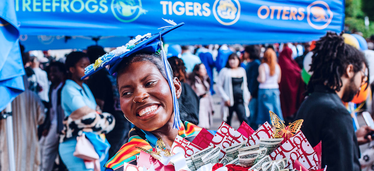 a smiling student in cap and gown holding a bouquet of flowers