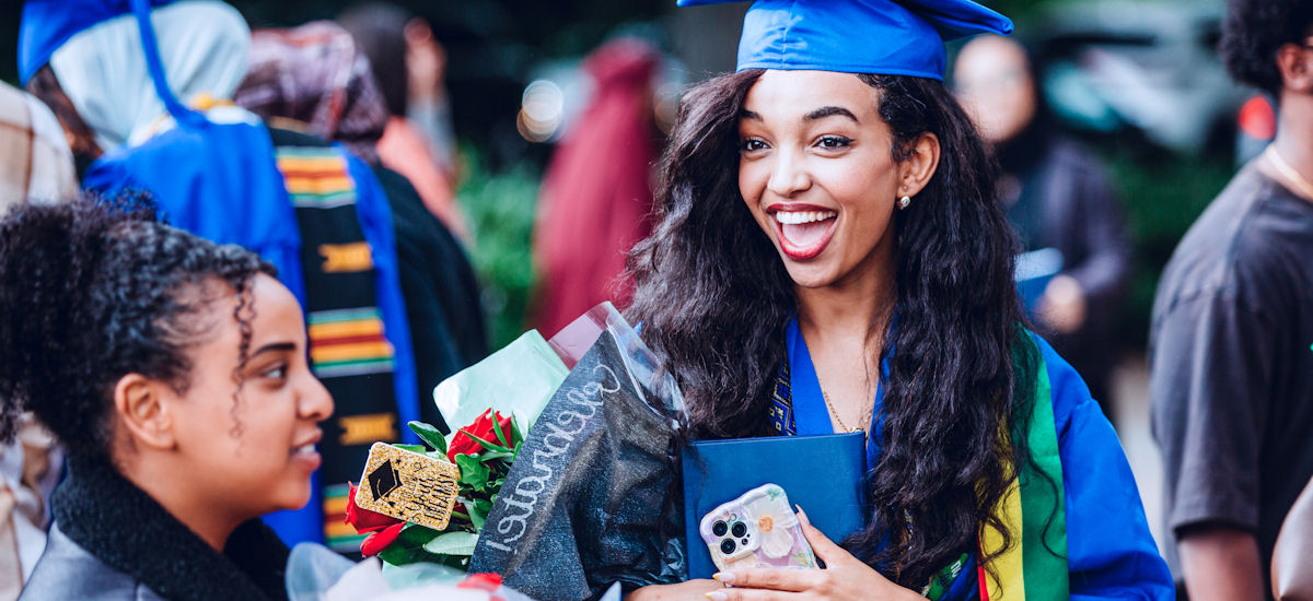 a smiling student in cap and gown holding a bouquet of flowers