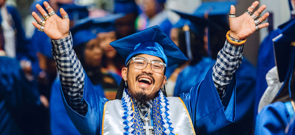 A student joyfully raising his arms before crossing the stage at commencement