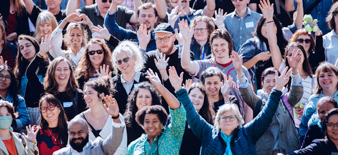 a large, diverse group of employees at North Seattle College smiling and raising their hands