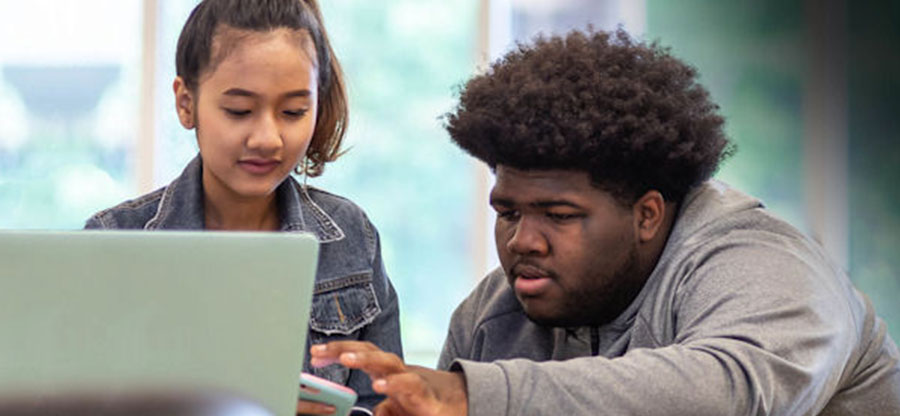 two students near a computer interacting over a cell phone