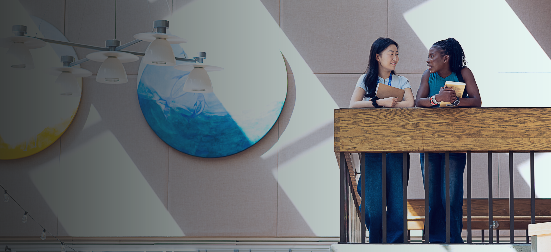 two women in conversation at the top of a stairwell landing with art in the background