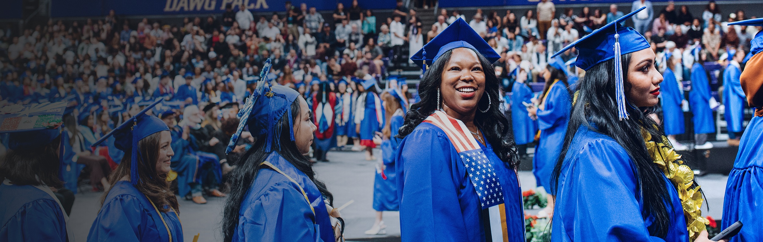smiling students in caps and gowns in a line-up to walk across the stage at commencement