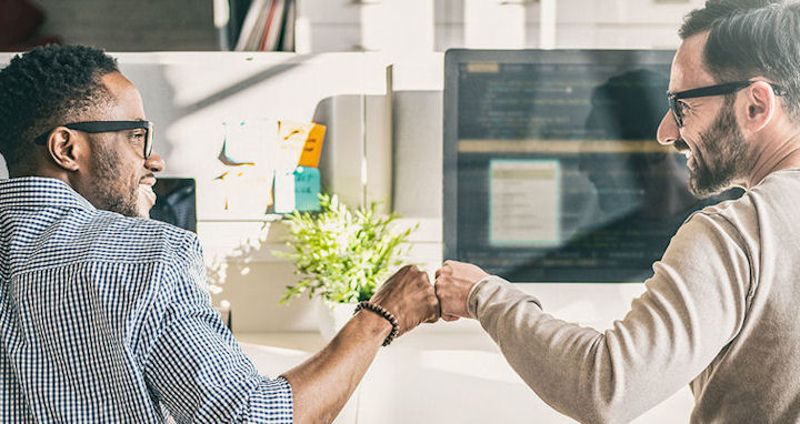 two people at computers giving a fist-bump and smiling