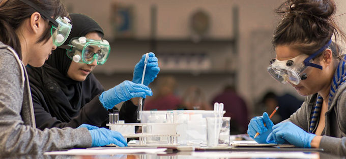 Students wearing safety goggles and gloves in a lab.