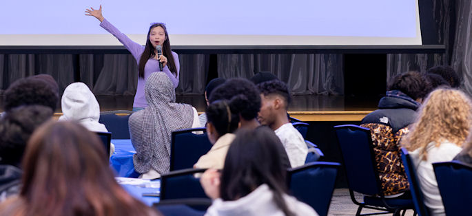a woman waving from the front of a room full of students