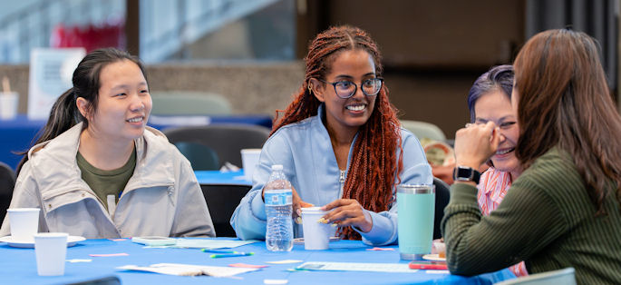 four diverse women smiling and interacting at a table