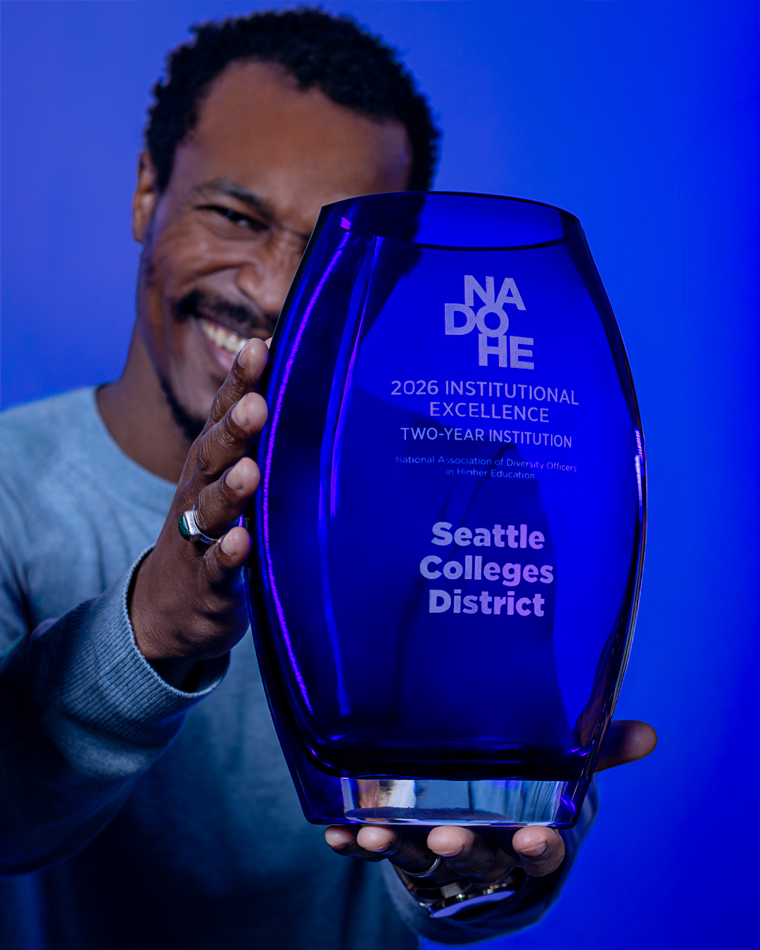 A staff member holding the 2026 NADOHE Institutional Excellence Award presented to Seattle Colleges
