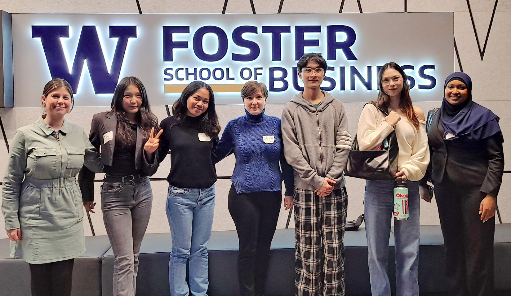 Mariyam Abdulkarim, Maila Jenner, Jane Madiz, Anna Kharzhevskaia, Khat Khongor, Michelle Sentevski, and Roger Tang standing as a group in front of the Foster School of Business sign