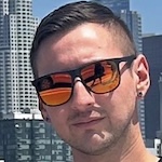 Close up on Julian Mena's face wearing sunglasses with cityscape in the background.